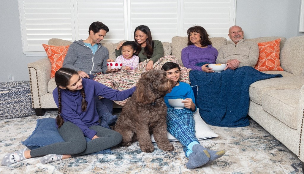 Large family sitting together on a sectional sofa with 2 kids and a dog sittin on the floor in front of the sofa